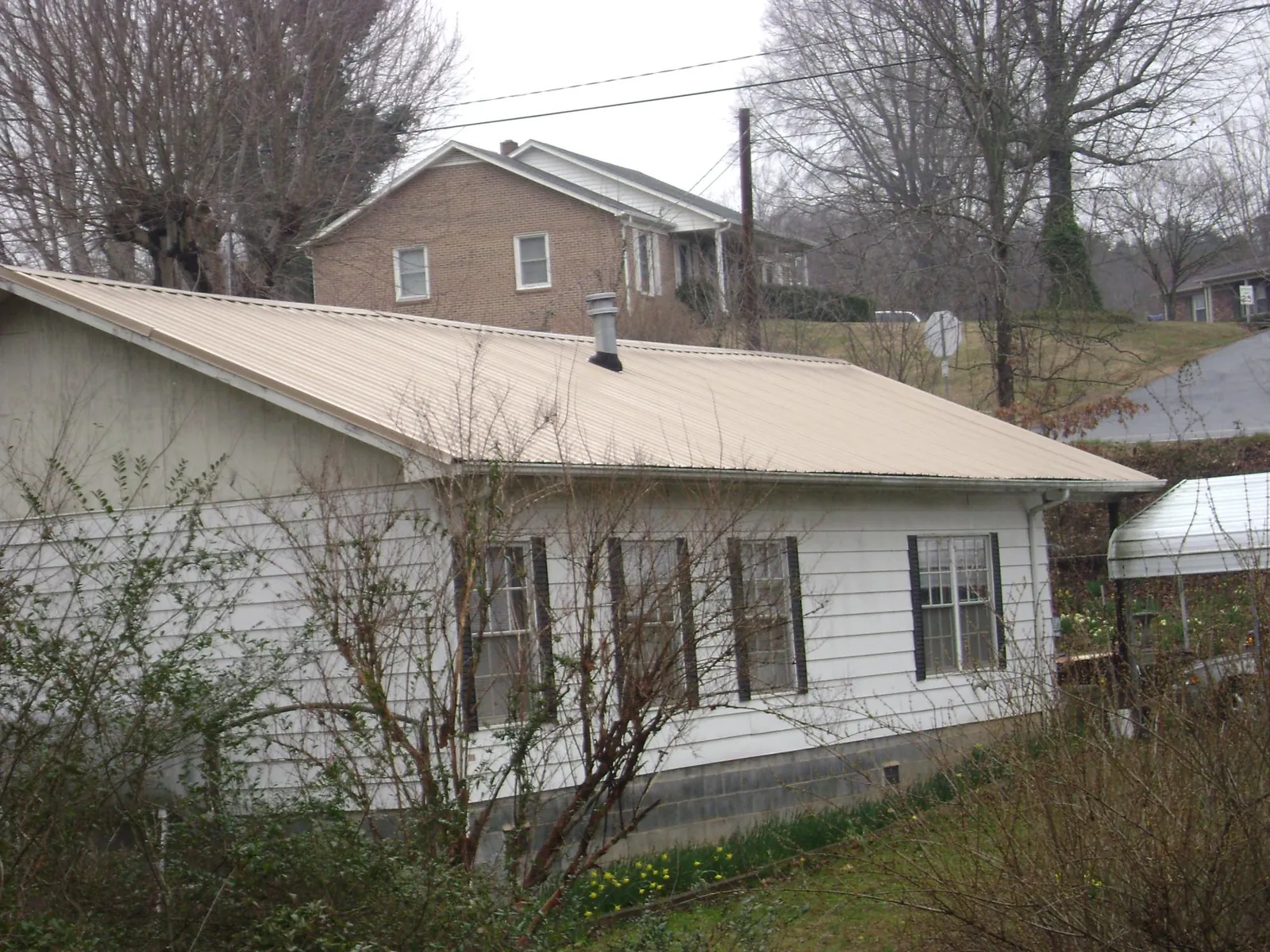 Tan metal roof on a white sided house set into a hillside — Commercial Roofing by Roofing Brothers in Clifton